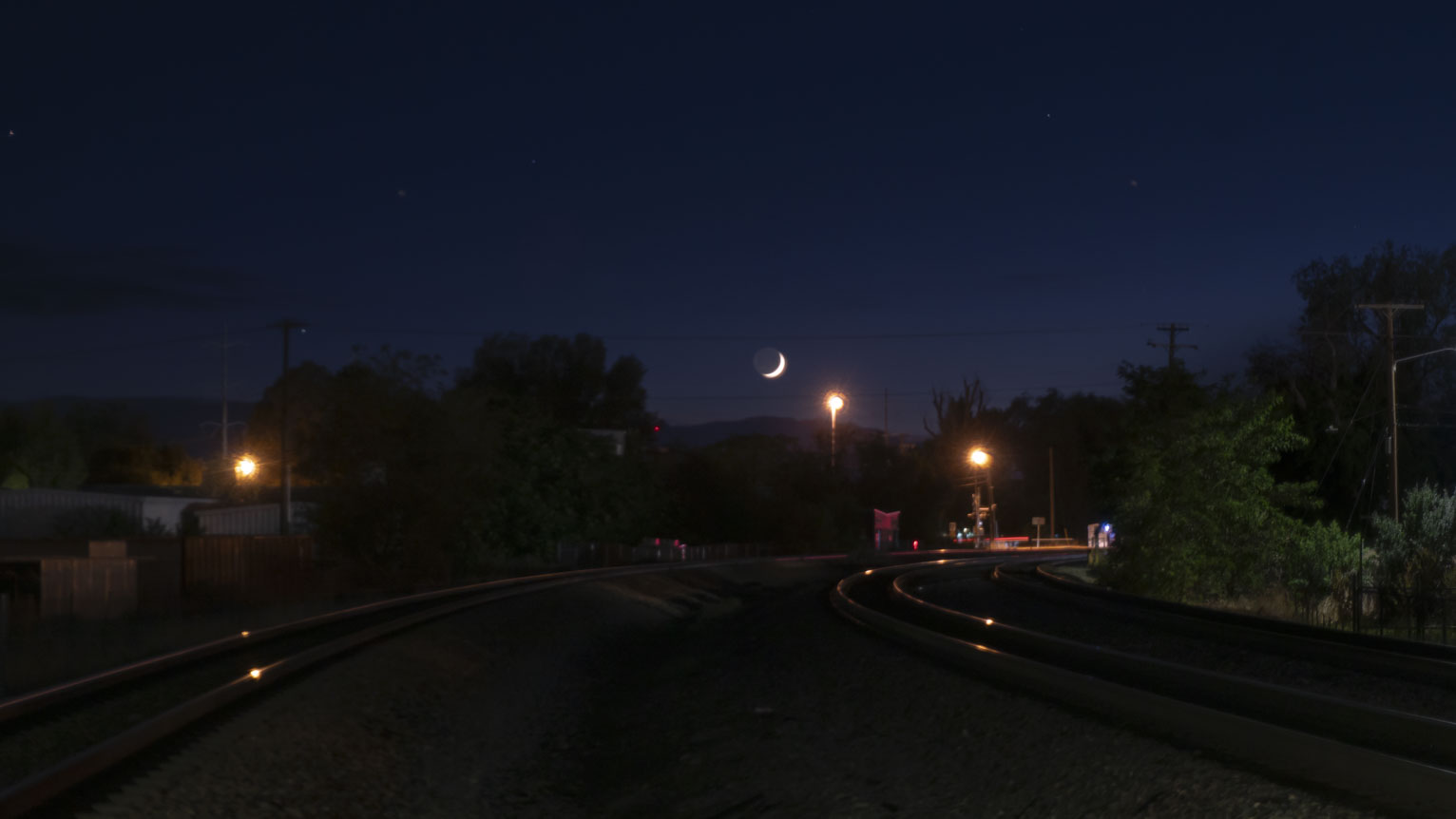 A crescent moon sets beyond the town train tracks